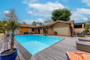 A swimming pool with a wooden deck, a covered patio area, and a garage. - La Farniente – Green House with Saltwater Pool, Close to the Médoc Beaches (Grayan-et-l'Hôpital)