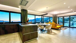 Une chambre d’hôtel moderne dotée d’un coin cuisine, d’un espace repas et de grandes fenêtres offrant une vue sur la ville.