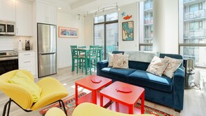 A modern apartment with a kitchen, dining area, and living room. It features a blue sofa, yellow chairs, and red tables.