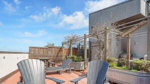 An outdoor patio with Adirondack chairs and a round table, surrounded by a wooden fence and potted plants.