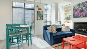 A modern living room with a blue sofa, teal chairs, a red table, and a fireplace.