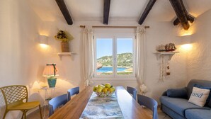 Un coin repas avec une table en bois, des chaises, un vase de fleurs et une vue sur la mer par la fenêtre.