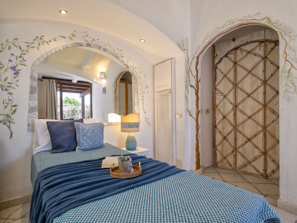 A bedroom with a bed, a bedside table with a lamp, and a decorative wall arch.