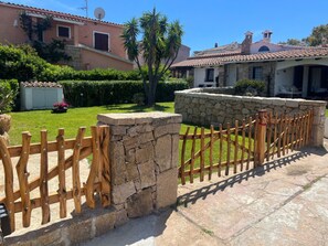 A stone wall with a wooden fence, a well-maintained lawn, and a building with a tiled roof.