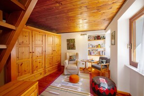 Een knus interieur met houten kasten, een comfortabele fauteuil, een klein tafeltje en een boekenkast.