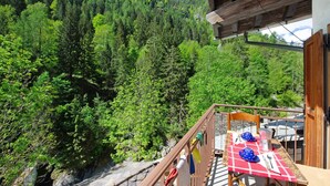 A wooden balcony with a table set for two, overlooking a forested mountain. - Holiday Home 'Casa Savin 35' with Mountain View, Private Garden and Balcony (Pontboset)