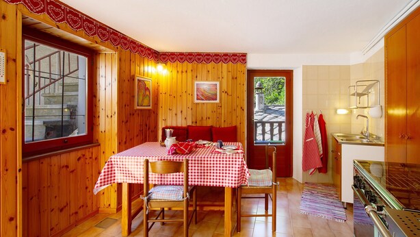 A wooden interior with a dining table set for two, a kitchen area, and a window with a view. - Holiday Home 'Casa Savin 35' with Mountain View, Private Garden and Balcony (Pontboset)