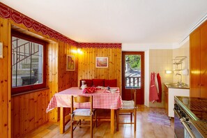 A wooden interior with a dining table set for two, a kitchen area, and a window with a view. - Holiday Home 'Casa Savin 35' with Mountain View, Private Garden and Balcony (Pontboset)