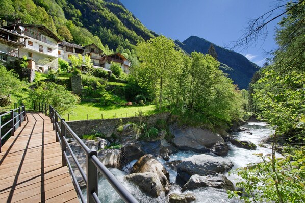 A wooden bridge over a river, surrounded by lush greenery and houses.