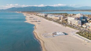 An aerial view of a coastal city with a beach, buildings, and mountains in the background. - Mobile Home 'Mobil-home Camping Mar Estang' with Lake View, Shared Pool & Air Conditioning (Canet-en-Roussillon)