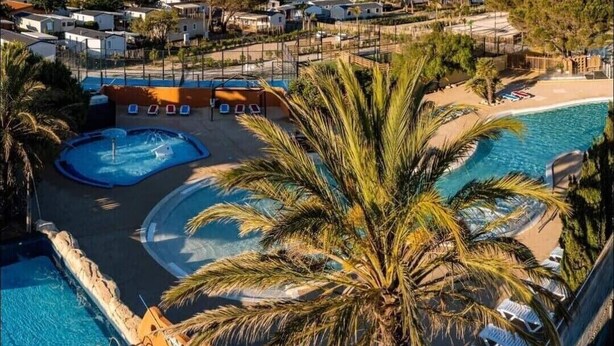 A resort with multiple swimming pools, palm trees, and a view of distant mountains. - Mobile Home 'Mobil-home Camping Mar Estang' with Lake View, Shared Pool & Air Conditioning (Canet-en-Roussillon)