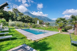 A swimming pool with a wooden deck, lounge chairs, and a view of mountains.