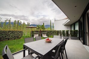 Une terrasse extérieure moderne, avec une table et des chaises, un saladier rempli de fruits et une vue sur les montagnes.
