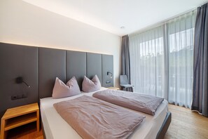 Une chambre d’hôtel moderne dotée d’un grand lit, de tables de chevet, d’un bureau et offrant une vue sur l’extérieur à travers de fines rideaux.