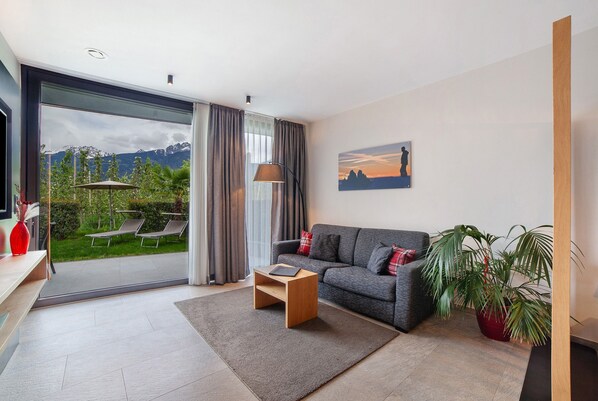 Un salon moderne avec un canapé, une table basse, une plante en pot et une vue sur un jardin, visible à travers une porte vitrée.