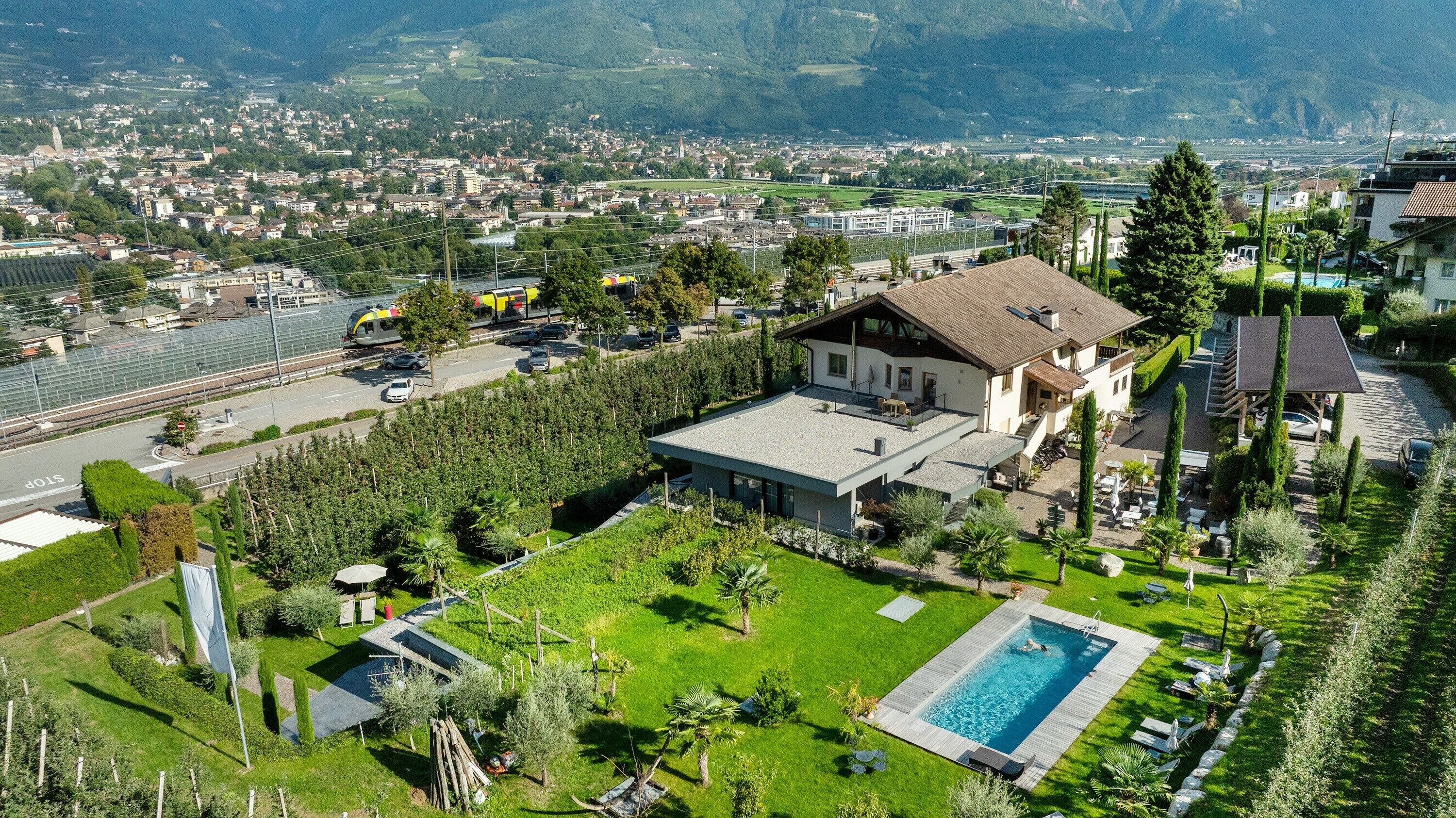 Una casa moderna amb piscina, envoltada de vegetació exuberant i vistes a una vila i muntanyes.