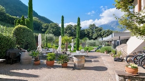 Une cour avec des espaces de repos en plein air, des plantes en pot et une vue sur les montagnes en arrière-plan.