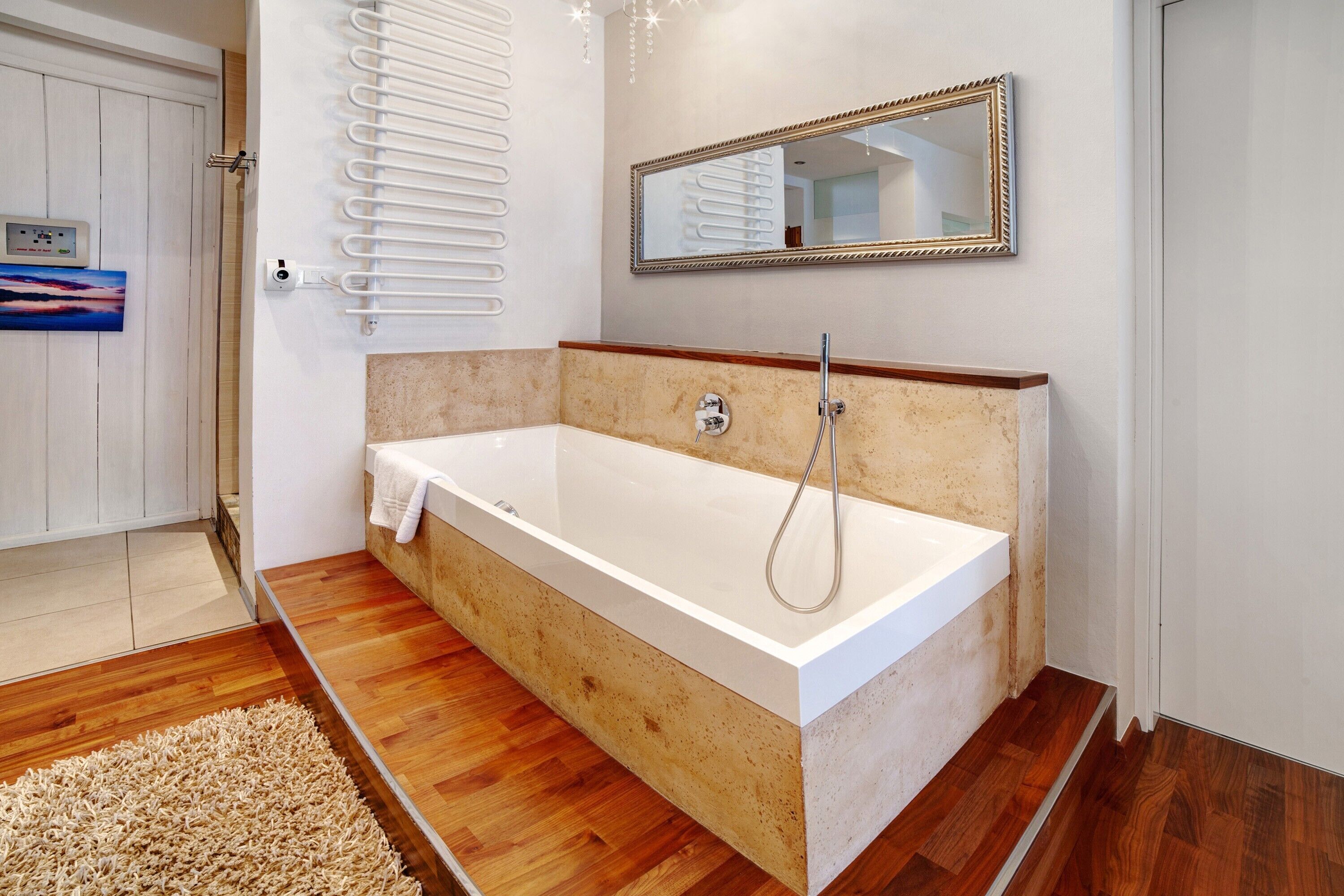 Une salle de bain moderne avec une baignoire sur pieds, un porte-serviettes mural, un miroir et un plancher en bois.