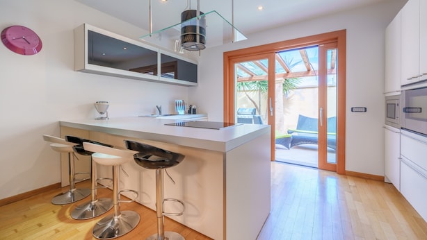 A modern kitchen with a central island, bar stools, a large window, and a sliding glass door leading to an outdoor area. - Dimora Smeralda Golfo Aranci – Central Location and Beach with Private Terrace (Golfo Aranci)