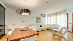 A modern living room with a wooden dining table, white sofa, and a unique white rocking chair. - Dimora Smeralda Golfo Aranci – Central Location and Beach with Private Terrace (Golfo Aranci)