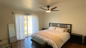 A bedroom with a bed, a ceiling fan, a window with curtains, and a wooden floor.