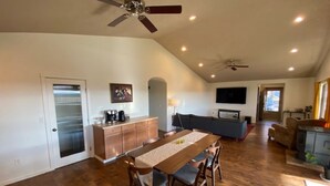 A spacious living area with a wooden dining table, chairs, a sofa, and a TV.