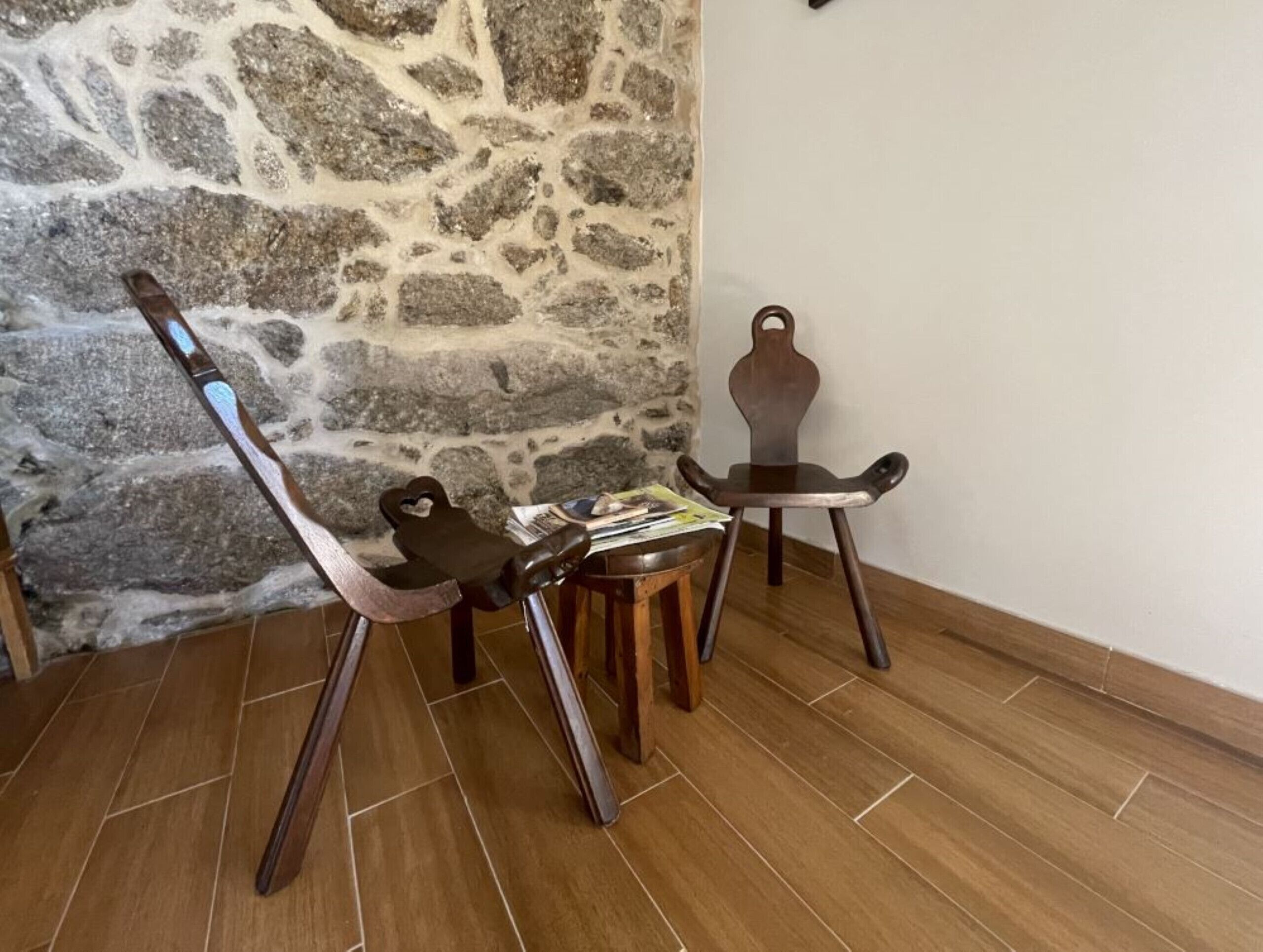 A room with a stone wall, a wooden floor, and two wooden chairs with heart-shaped backrests.