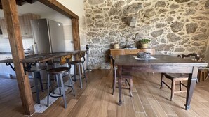 A rustic kitchen with a stone wall, wooden table, and bar stools. - YourHouse A Casa Da Corona, beautiful country house (Ourense)