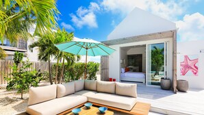 Un espace de vie extérieur moderne avec un canapé d’angle beige, une table basse en bois et un parasol turquoise.