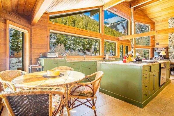 A spacious kitchen with large windows, a dining area with wicker chairs, and a stone accent wall.