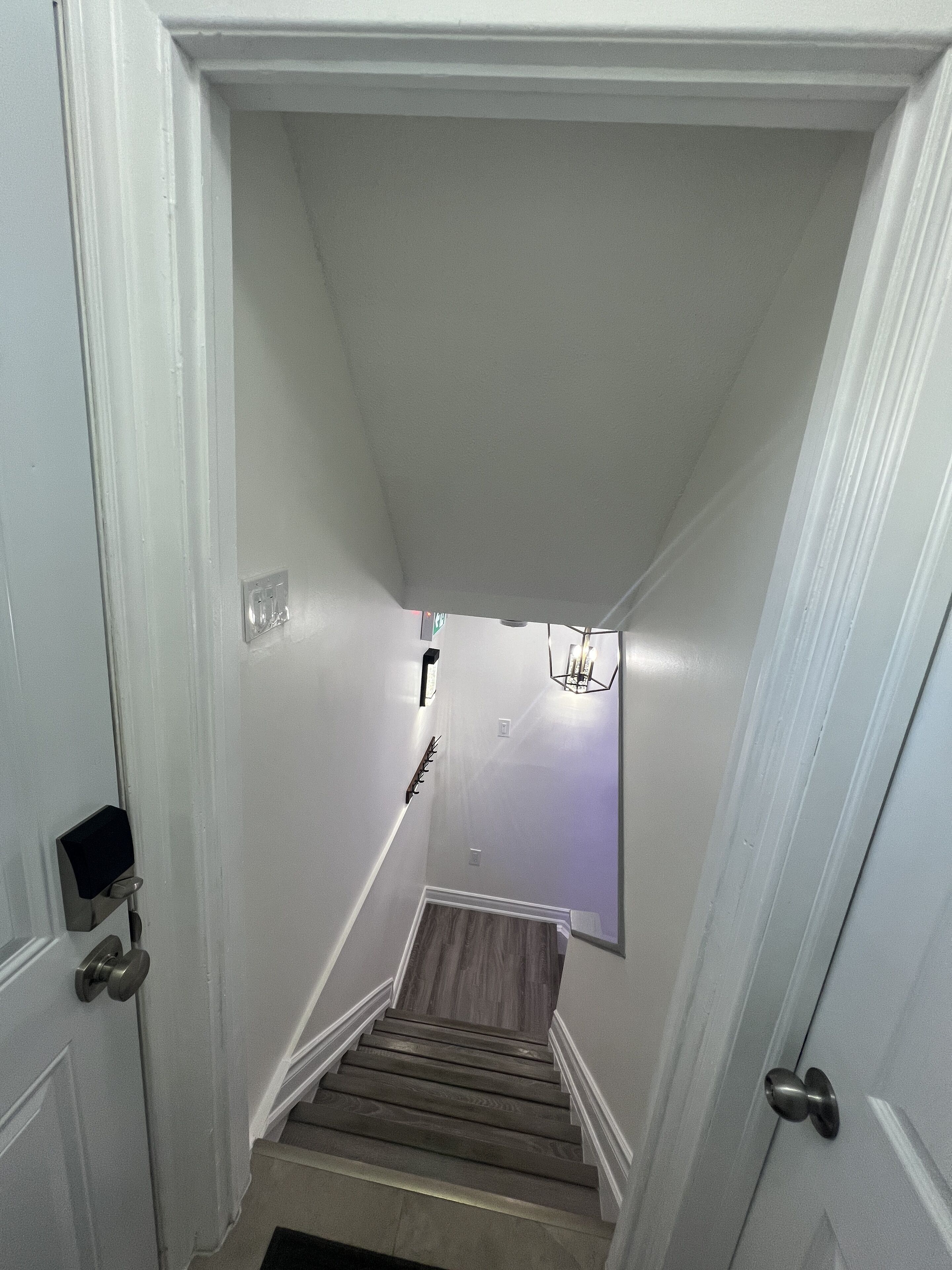 A narrow stairway with a wooden handrail and a light fixture at the top.