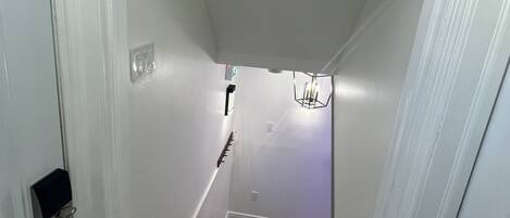 A narrow stairway with a wooden handrail and a light fixture at the top.