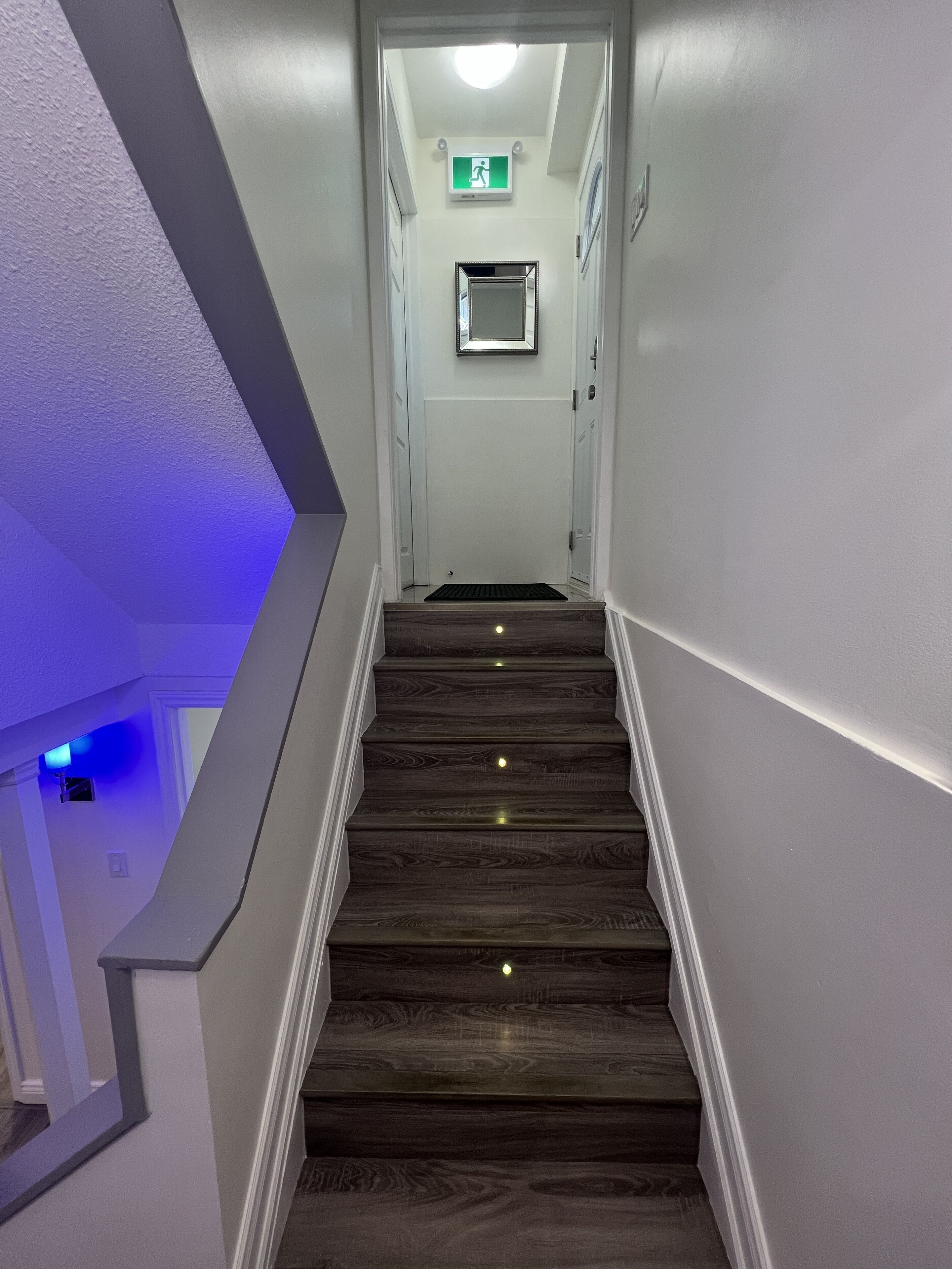 A staircase with wooden steps and a handrail, leading to a door with an emergency exit sign.