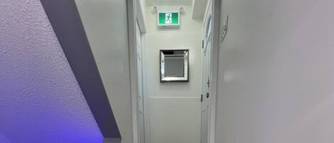 A staircase with wooden steps and a handrail, leading to a door with an emergency exit sign.