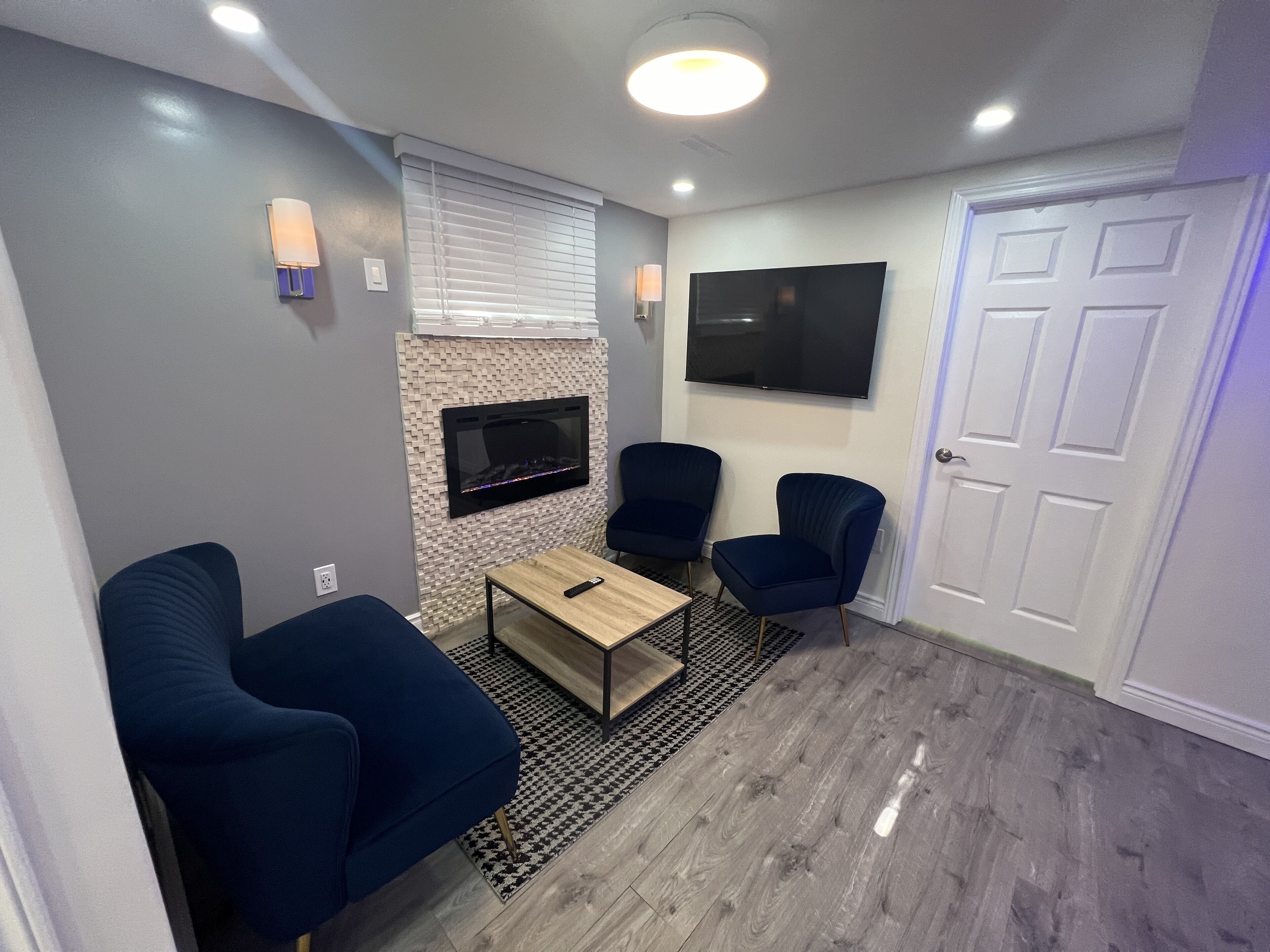 Una sala moderna con chimenea, dos sillones azules, una mesa de centro, un televisor montado en la pared y una alfombra estampada.