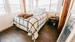 Een slaapkamer met een bed, nachtkastje, lamp en uitzicht.
