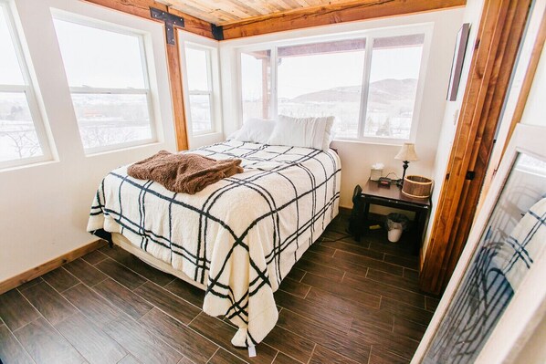 Une chambre à coucher avec un lit, une table de chevet, une lampe et une vue sur l’extérieur.