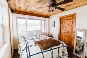 Un dormitorio con cama, una puerta de madera, una ventana y un ventilador de techo.