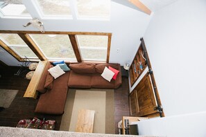 Una habitación amplia con un sofá seccional marrón grande, un banco de madera y un tragaluz.