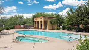 Une piscine avec un jacuzzi, un pavillon couvert et un espace clos équipé de chaises longues.