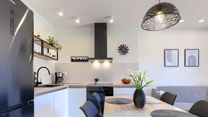 Una cocina moderna con refrigerador empotrado, cafetera y comedor con mesa y sillas de madera.