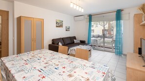 Quarto com cama, sofá, mesa e televisão. Janela com vista para a rua.