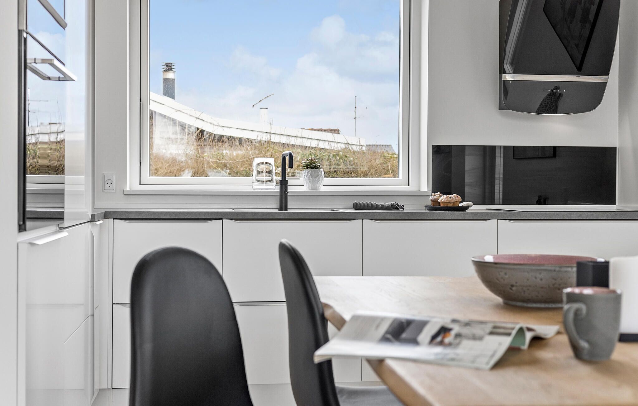 Een moderne keuken met witte kastjes, een zwarte kraan en een raam met uitzicht op het landschap.