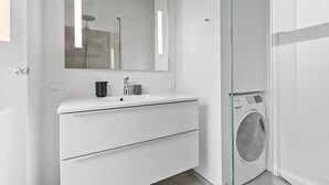 Un baño moderno con tocador blanco, un espejo, ducha y lavadora integrada.