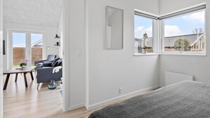 Una habitación moderna con una cama grande, un escritorio y una silla. Hay dos ventanas con vistas al exterior.