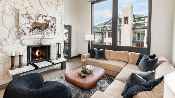 A modern living room with a stone fireplace, a large window with a view of buildings, and a cozy seating area.