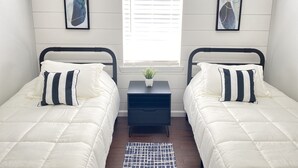 A bedroom with two beds, a small table with a plant, and a window with blinds. - Gem of Jacksonville, near NC Beaches & Military Base (Jacksonville)