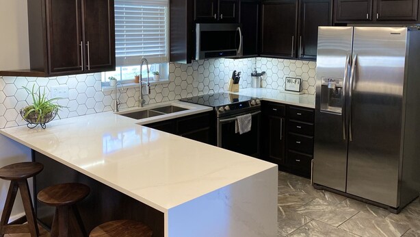 A modern kitchen with dark cabinets, a white island with stools, stainless steel appliances, and a hexagonal tile backsplash. - Gem of Jacksonville, near NC Beaches & Military Base (Jacksonville)