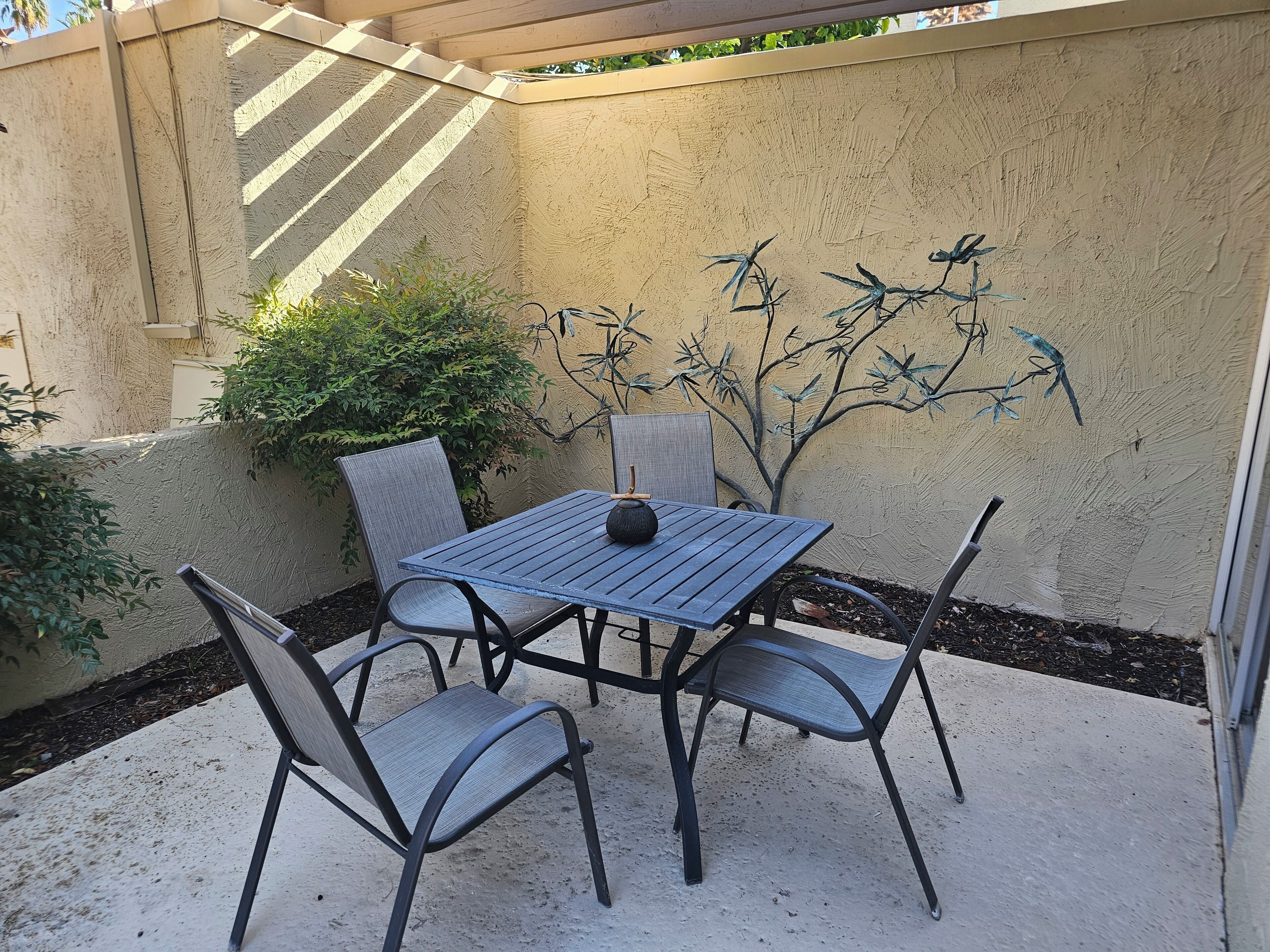 A patio with a table and chairs, surrounded by a textured wall and greenery.