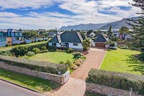A residential area with modern houses, a well-maintained lawn, and a mountain in the background. - Fairview Hermanus | Ocean View Home, Sleeps 8 (Hermanus)